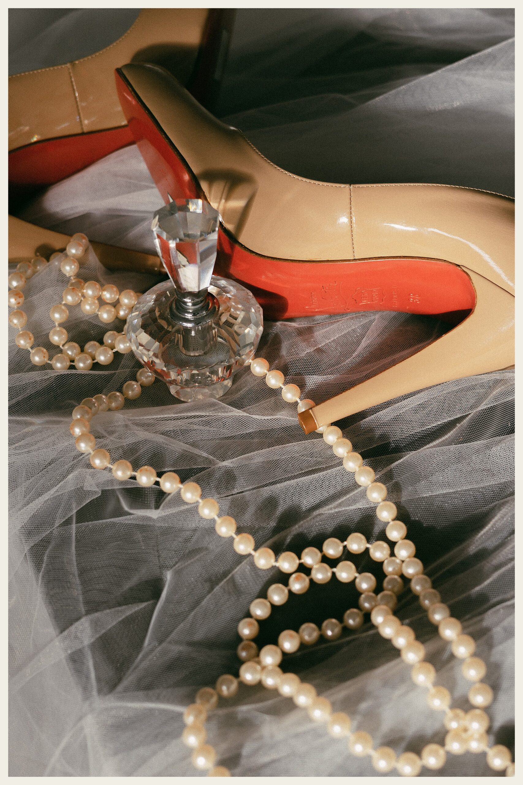 louboutin shoe with perfume bottle and pearl necklace